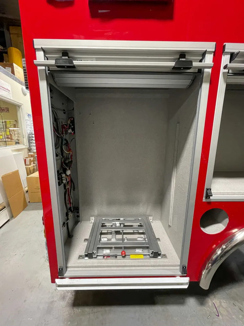 Exterior view of small fire truck showing cab, body compartments, and wheel/tire area.